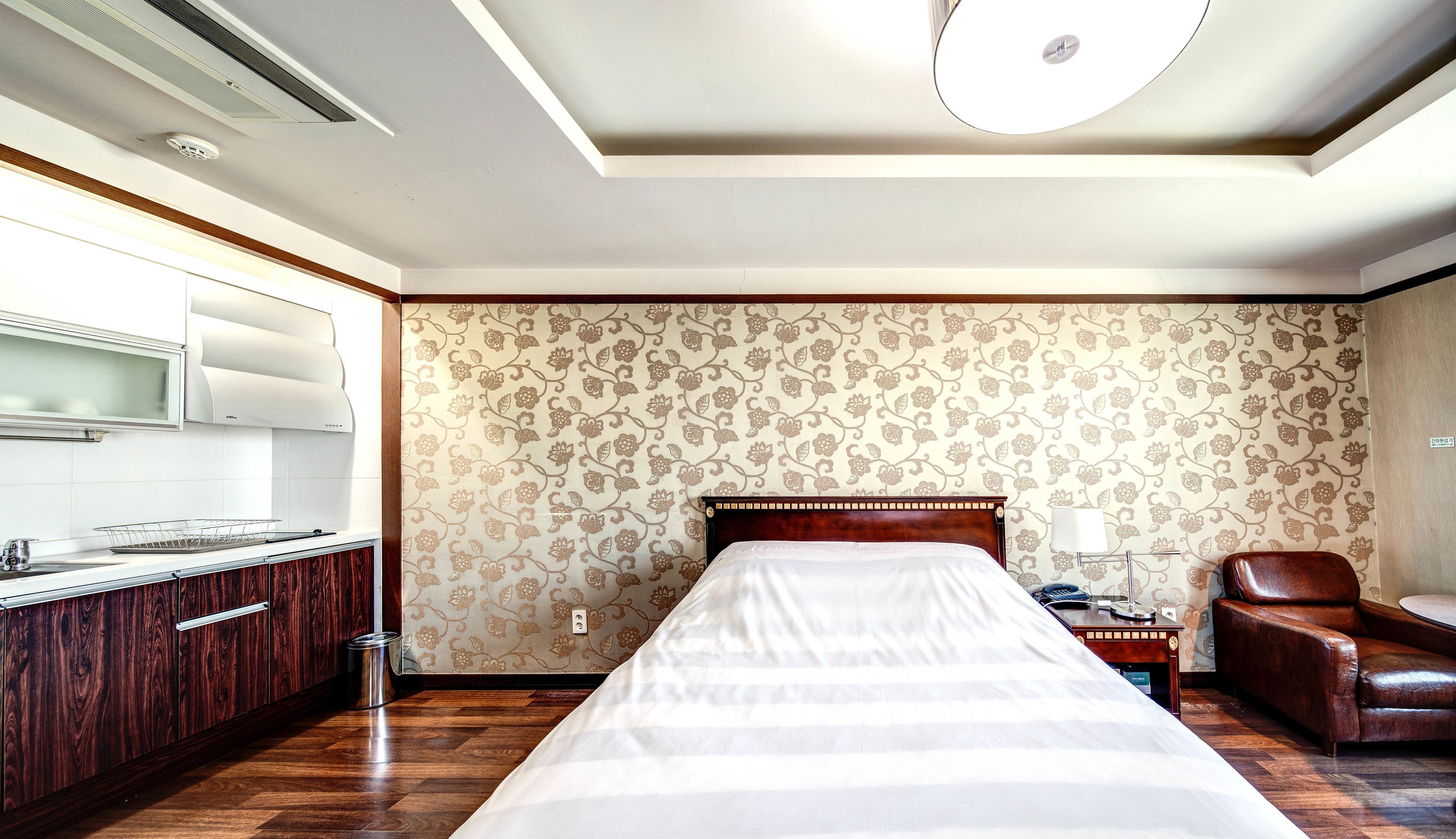 Una habitación de hotel con una cama grande, un aparador de madera, una silla, una mesita de noche y una pared con papel tapiz floral.