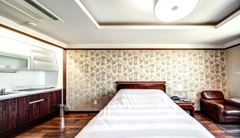 Una habitación de hotel con una cama grande, un aparador de madera, una silla, una mesita de noche y una pared con papel tapiz floral.