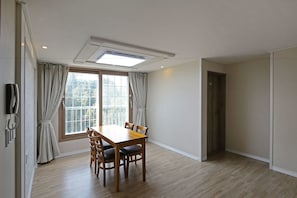 En matplats med ett träbord och stolar, ett stort fönster med gardiner och en taklampa.