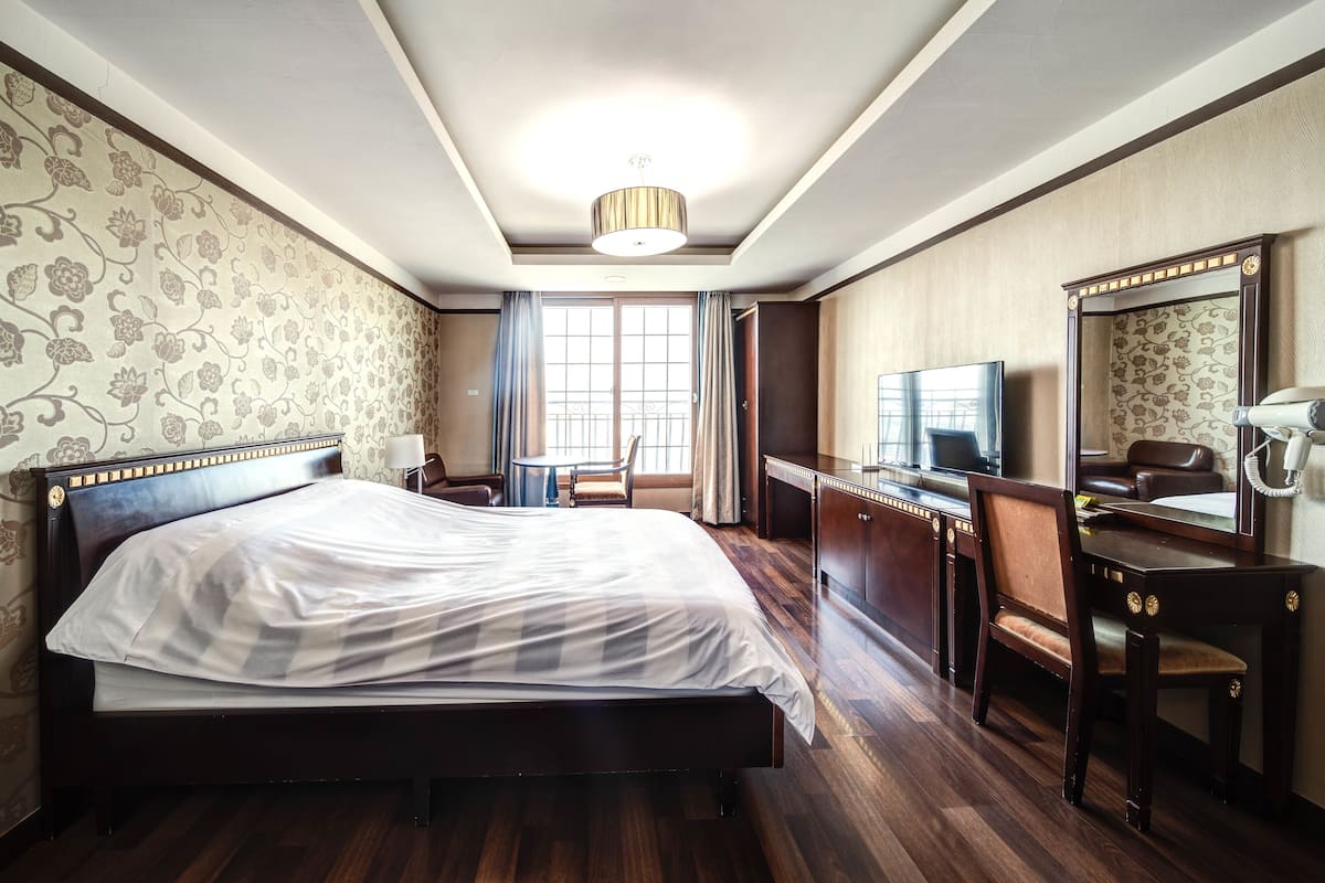 A hotel room with a large bed, a desk, a chair, a television, and a mirror.