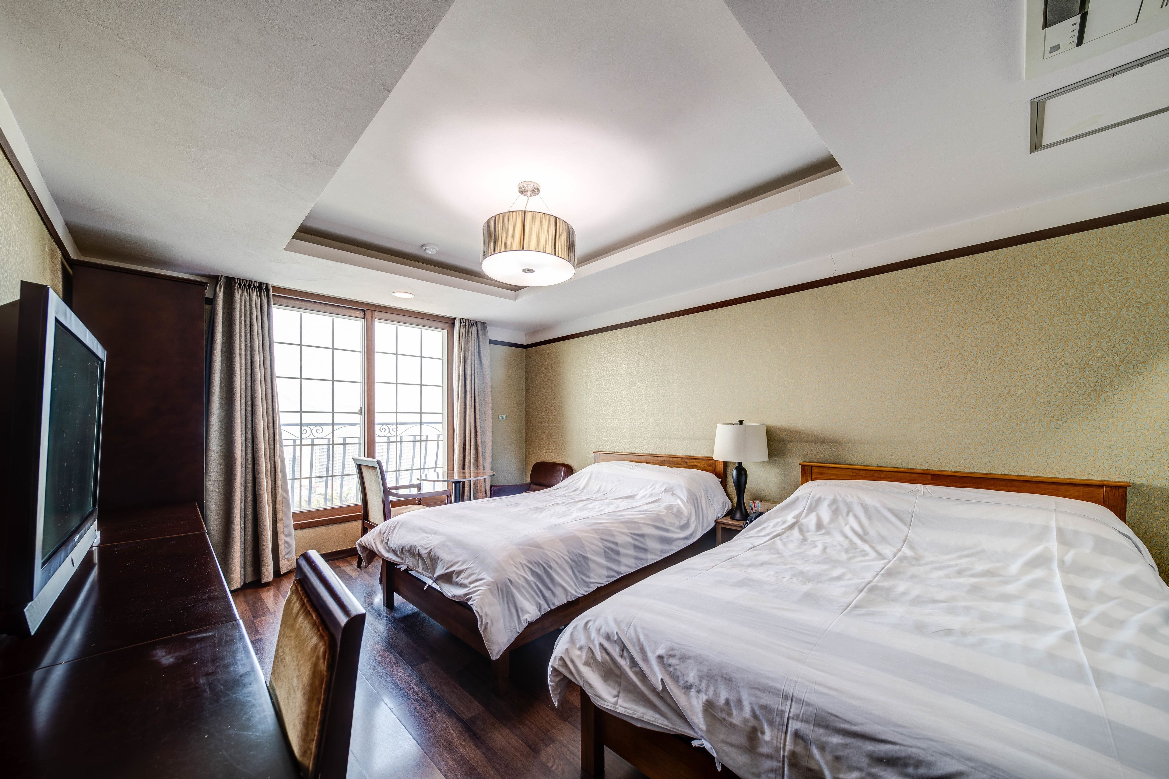 A hotel room with two beds, a television, a desk, and a window with curtains.