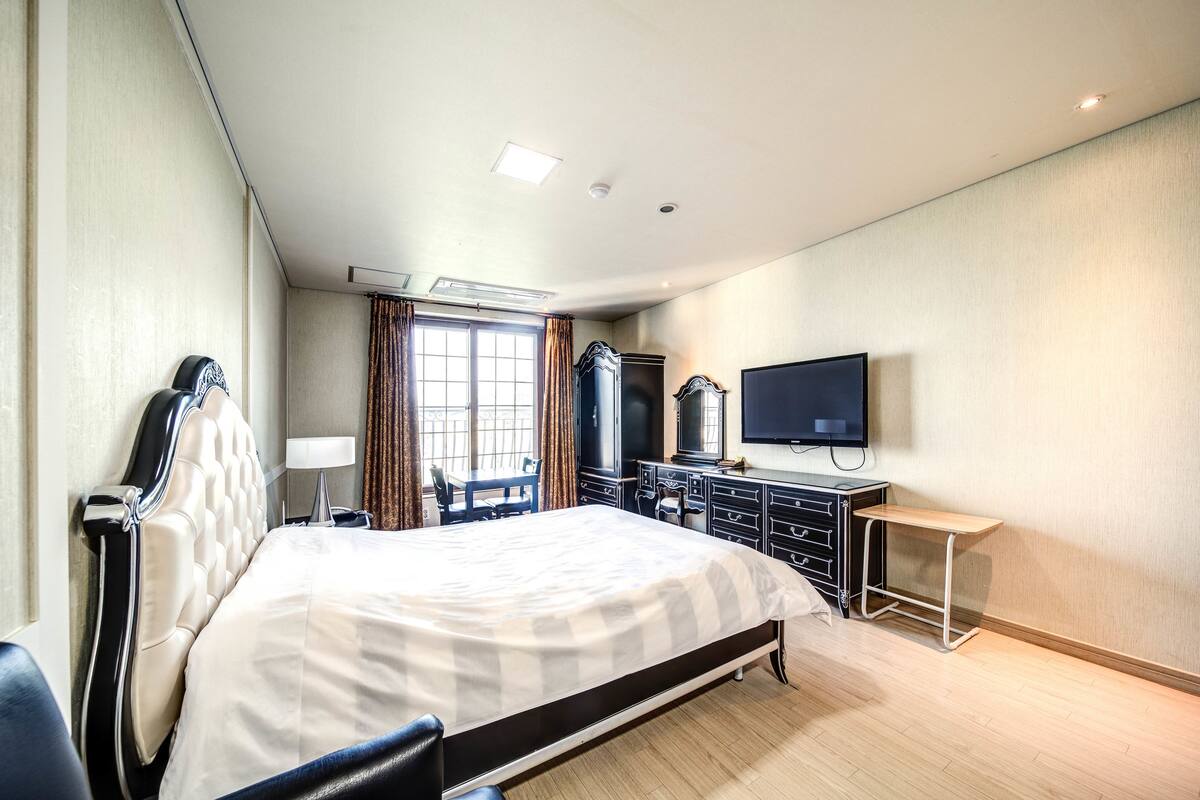 A hotel room with a large bed, a desk, a TV, and a wardrobe.