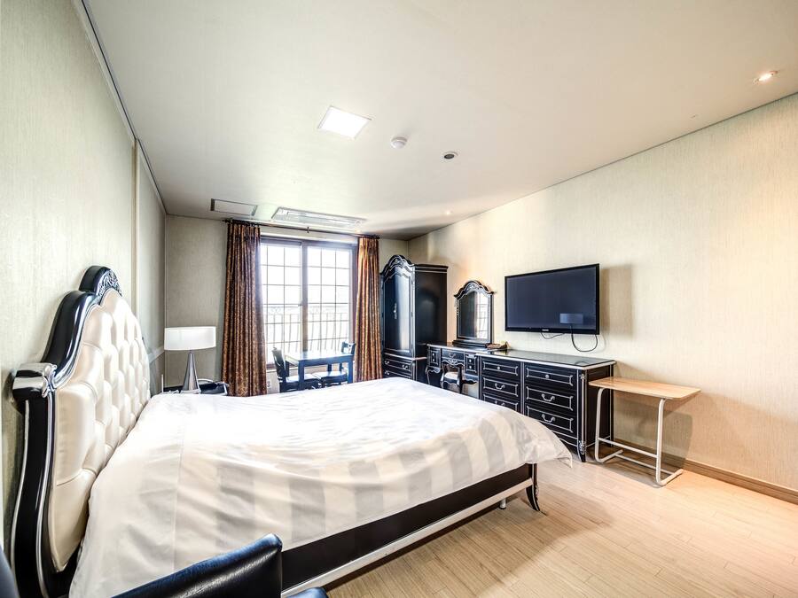A hotel room with a large bed, a desk, a TV, and a wardrobe.