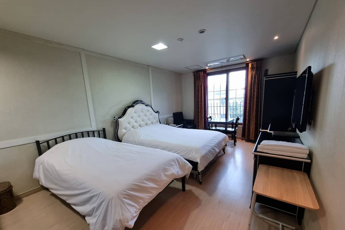 A hotel room with two beds, a desk, a chair, a TV, and a window with curtains.