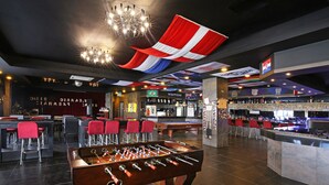 Zona de bar con mesa de fútbol de mesa, taburetes de bar rojos y mesa de billar.