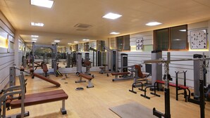 Un gimnasio con diversos equipos de ejercicio, espejos y suelo de madera.