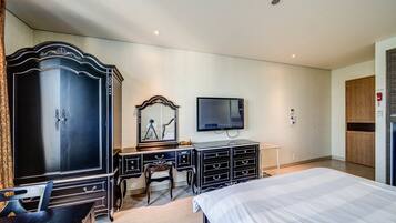 Habitación de hotel con una cama grande, un escritorio con cajones, una silla, un armario, un espejo y un televisor de pantalla plana montado en la pared.