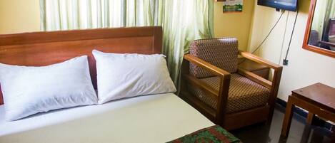 Una habitación de hotel con una cama, una silla, un televisor y una mesita.