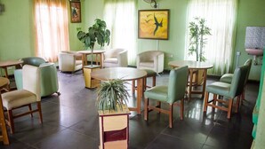 A spacious room with a round table, several chairs, a small bookshelf, and two large potted plants. - Allonze Hotel (Ikorodu)