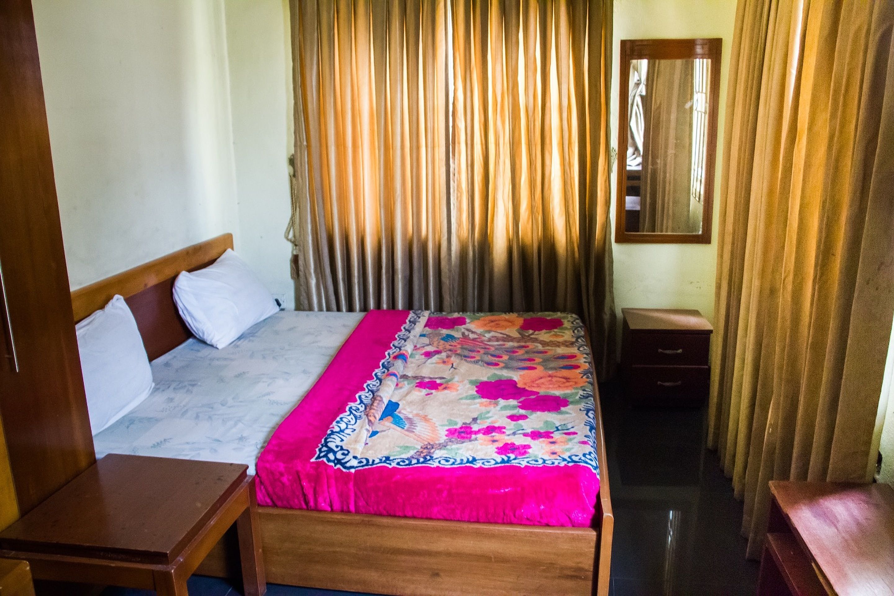 Una habitación de hotel con una cama de madera, una mesita de noche, un tocador y un espejo.