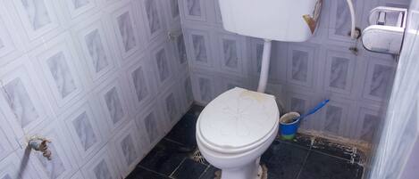Egy kis, egyszerű fürdőszoba, amelyben egy WC, egy kék vödör és egy kézi szivattyú található.