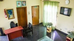 A reception area with a desk, chairs, a fire extinguisher, framed pictures, a clock, and a television. - Allonze Hotel (Ikorodu)