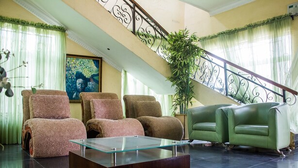 A spacious living area with a glass coffee table, patterned sofas, and a staircase with a decorative railing. - Allonze Hotel (Ikorodu)