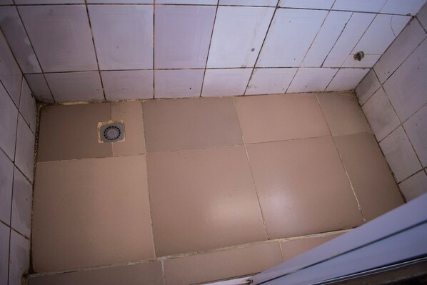 A tiled bathroom with a drain in the center. - Bavidi Hotel (Lagos)