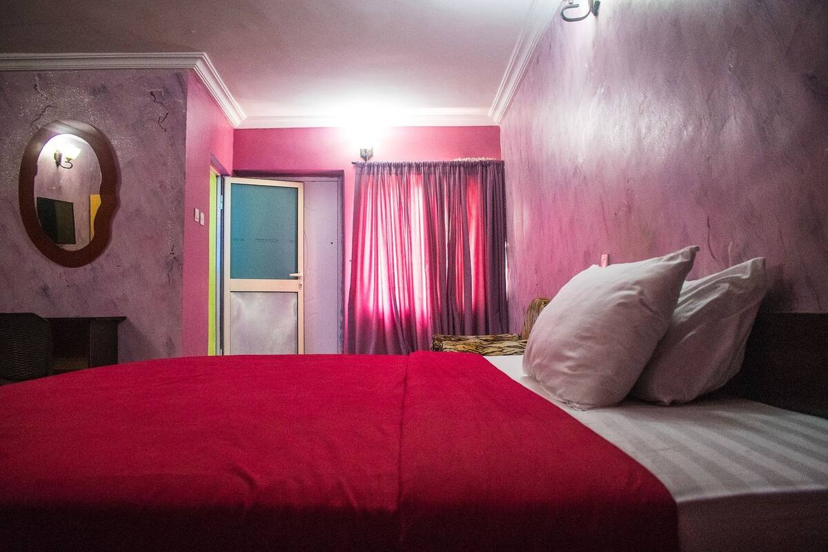 Une pièce avec un lit, un miroir, une porte et des rideaux.