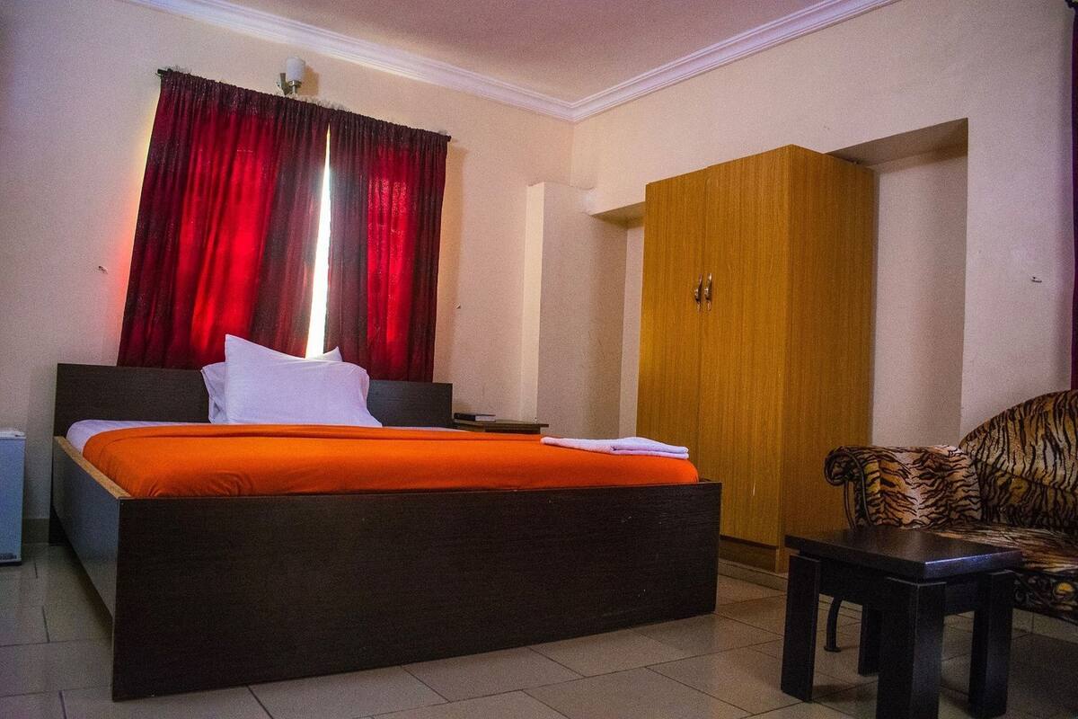 Une chambre d’hôtel avec un lit, une armoire en bois, une chaise et un rideau rouge.