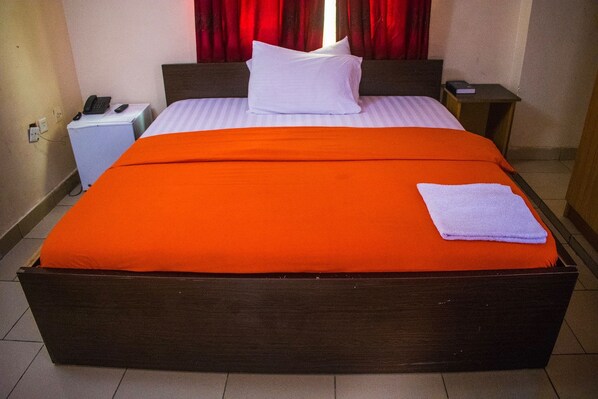 Una habitación de hotel con una cama grande, una mesita de noche con un teléfono y otra mesita con un libro.