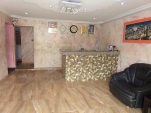 A lobby with a reception desk, a black leather sofa, a chandelier, and clocks labeled 'LONDON' and 'NIGERIA'. - Bavidi Hotel (Lagos)