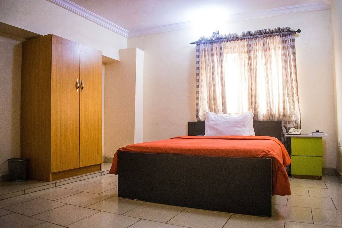 Une chambre à coucher avec un lit, une armoire, une table de chevet et une fenêtre avec des rideaux.