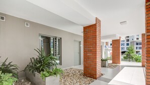 Un edificio moderno con un diseño limpio y minimalista, que combina elementos de ladrillo y concreto, un área exterior amplia con piso de baldosas y plantas en macetas.