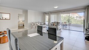 Una sala de estar moderna con comedor, ventanas amplias y un balcón con mobiliario exterior.