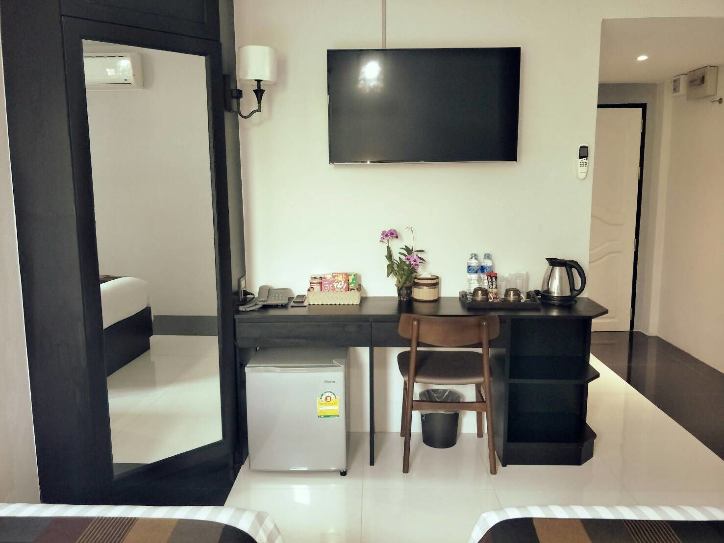 A hotel room with a bed, a desk with a chair, a television, a mini-fridge, a coffee maker, and a trash bin.