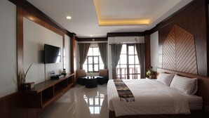 Una habitación de hotel moderna con una cama grande, un televisor de pantalla plana, un espacio de descanso con una mesita y ventanas amplias con cortinas.