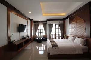 Una habitación de hotel moderna con una cama grande, un televisor de pantalla plana, un espacio de descanso con una mesita y ventanas amplias con cortinas.