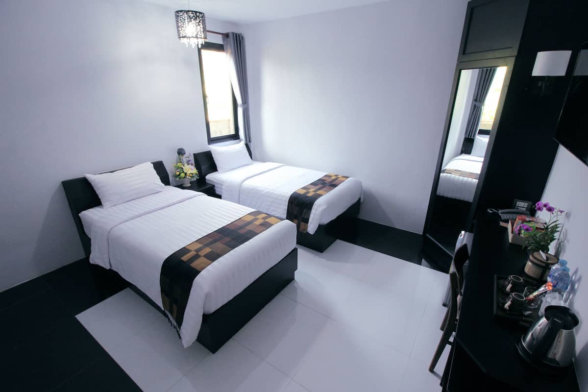 A hotel room with two beds, a small table with a kettle, and a mirror.