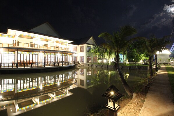 A waterfront hotel with a reflection in the water, a walkway, and palm trees.