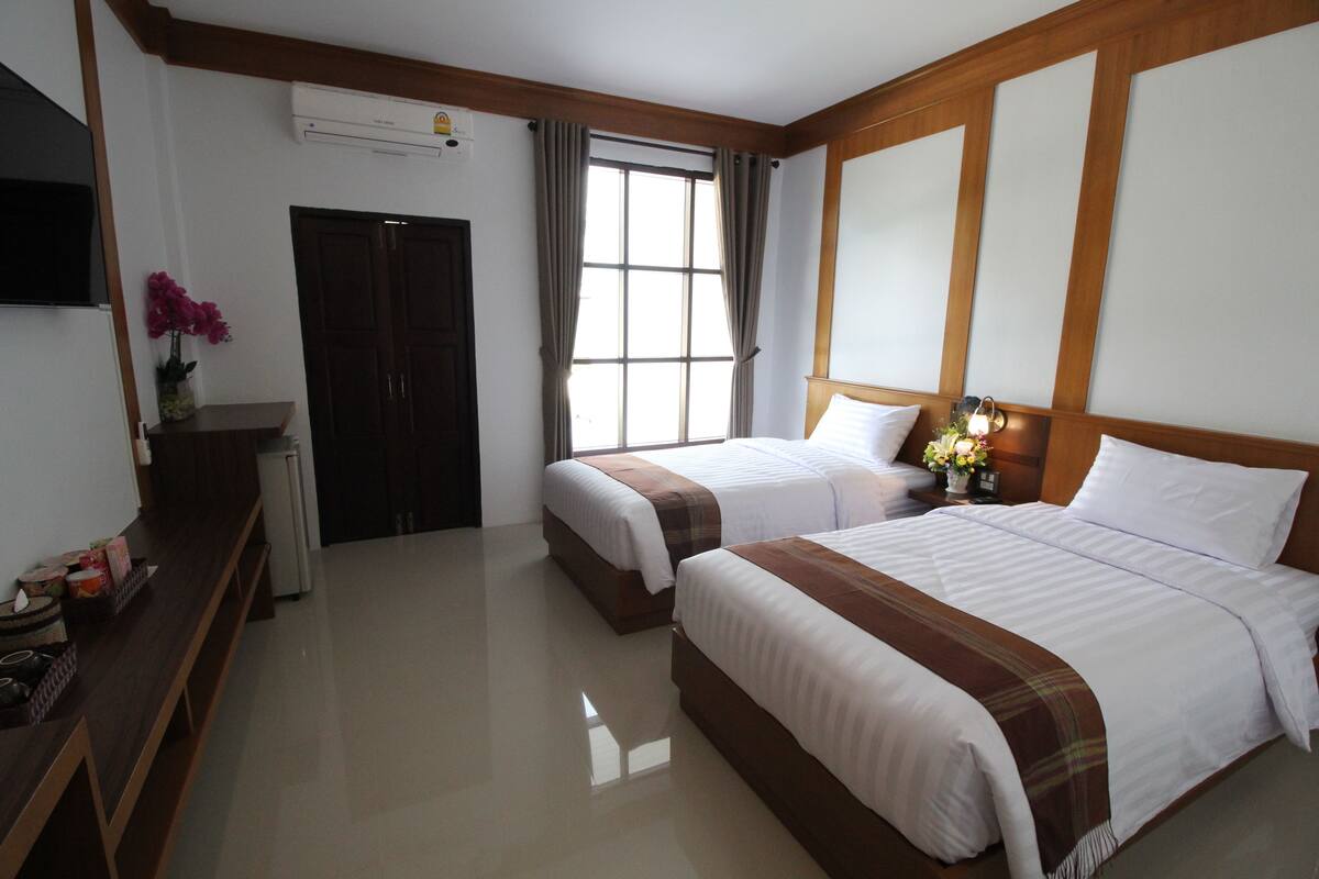 A hotel room with two beds, a TV, a desk, and a window with curtains.