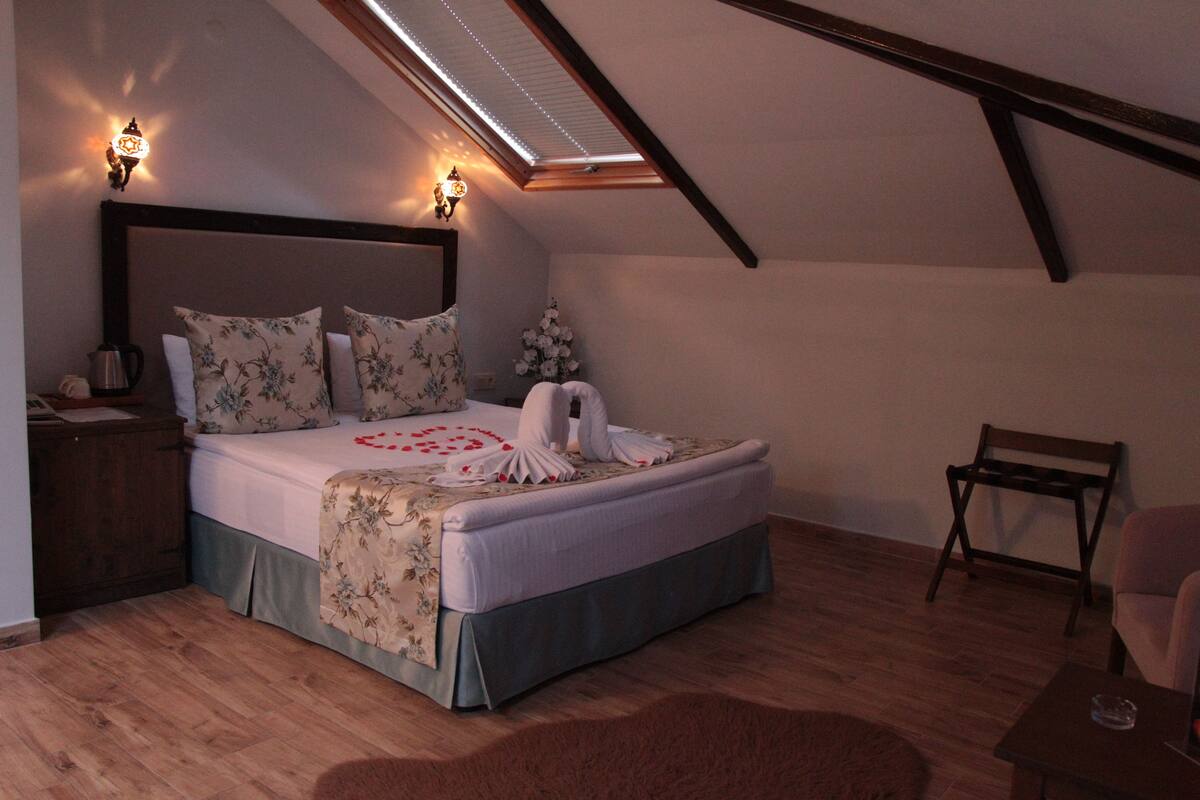 A bedroom with a sloped ceiling, a bed with floral bedding, two wall-mounted lights, a wooden nightstand, and a chair.