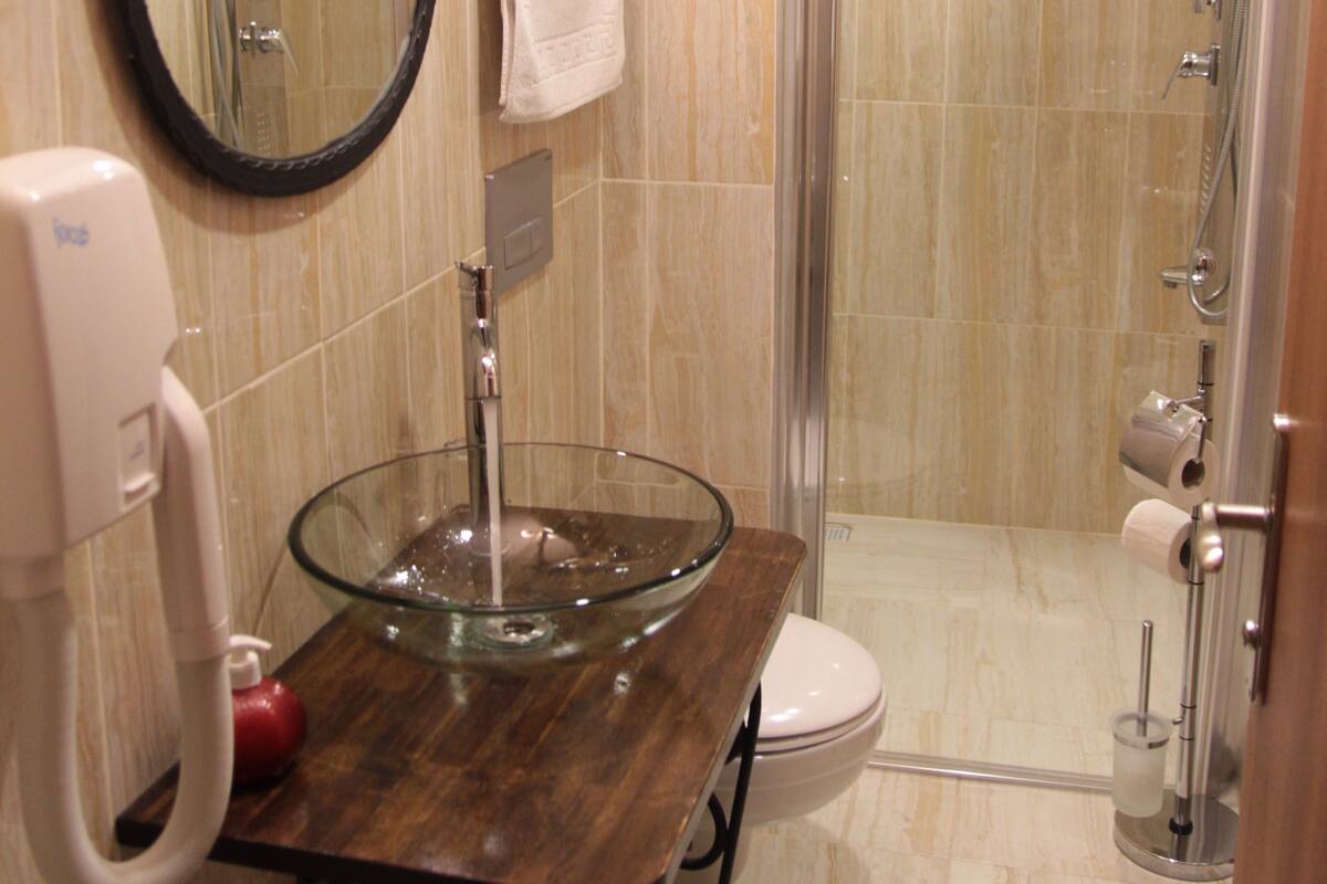 A bathroom with a glass sink, a mirror, a toilet, and a shower enclosure.