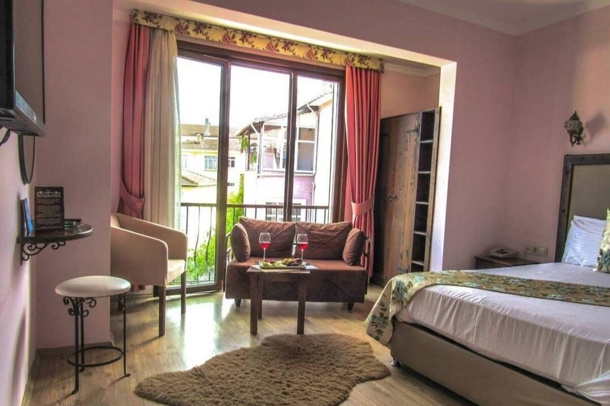 A bedroom with a bed, a sofa, a small table with glasses, a rug, and a window with curtains.