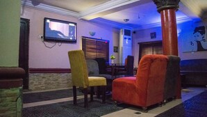 Eine Lobby mit Wandfernseher, roter Säule und einer Sitzecke mit Sesseln.
