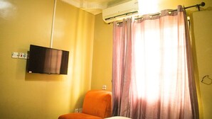 Ein Hotelzimmer mit einem Bett, einem orangefarbenen Sessel, einem an der Wand montierten Flachbildfernseher und einem Fenster mit violetten Vorhängen.