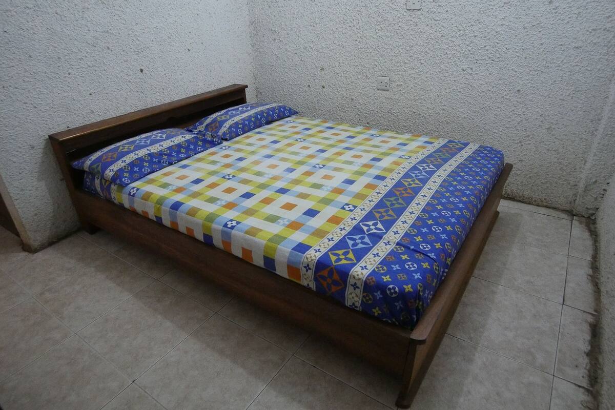 Un lit simple avec une couvre-lit à motifs et des oreillers, une tête de lit en bois et un mur à texture.