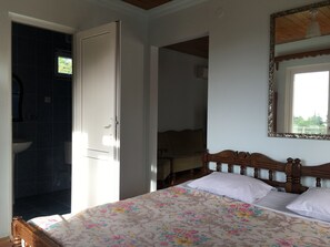 A bedroom with a bed, a wooden headboard, a mirror, and a bathroom with a sink and dark tiles. - White Guest House (Batumi)