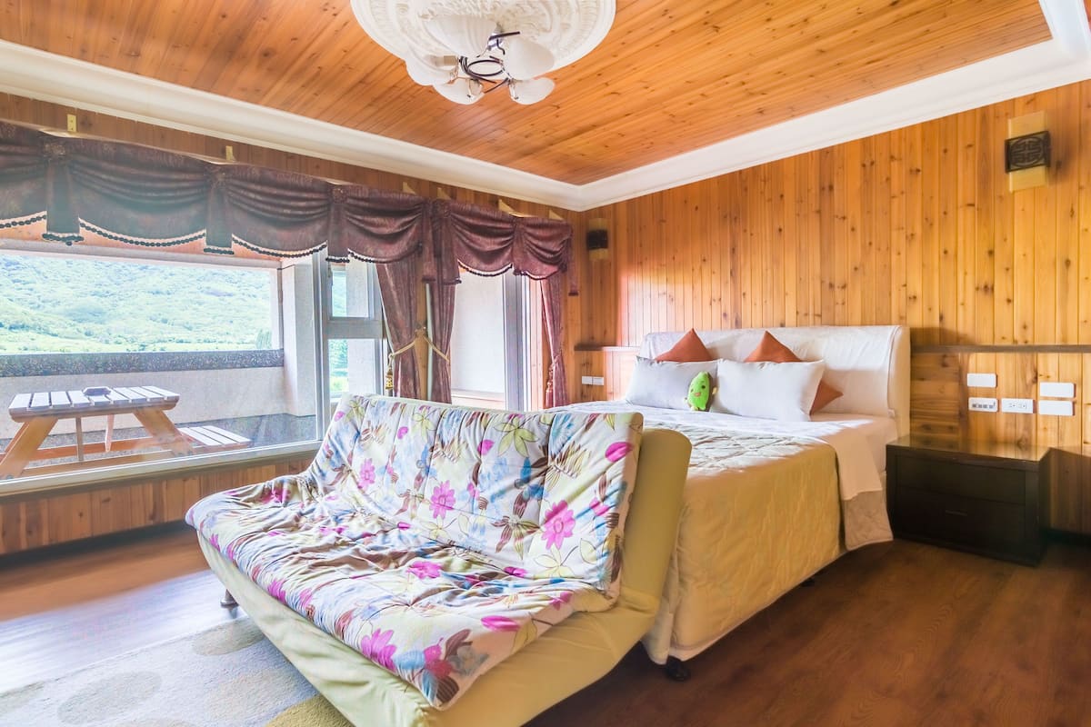 A wooden-paneled room with a bed, a sofa, and a window overlooking a scenic view.