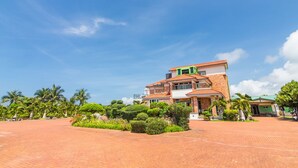 A two-story building with a red-tiled roof, surrounded by landscaped gardens and palm trees. - Kenting Maya House B&B (Hengchun)