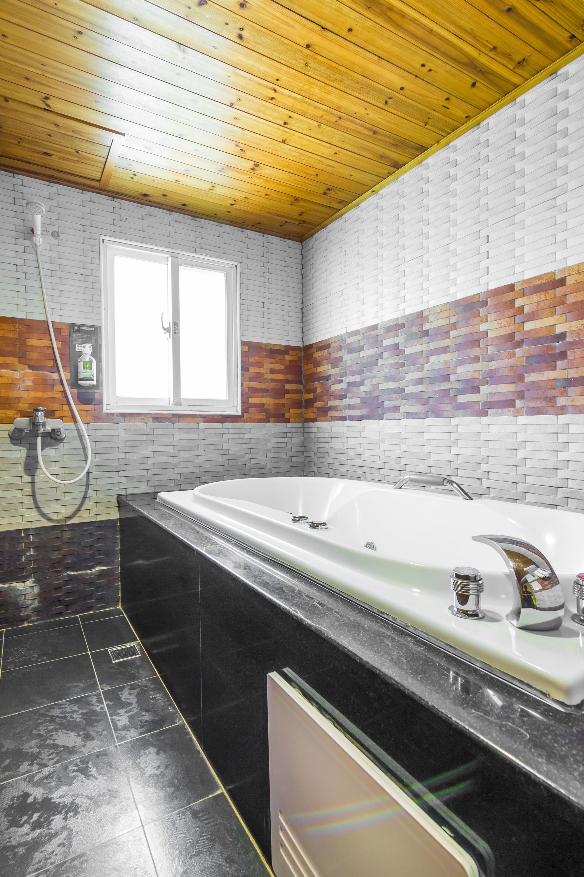 A bathroom with a white bathtub, a window, and a shower area.