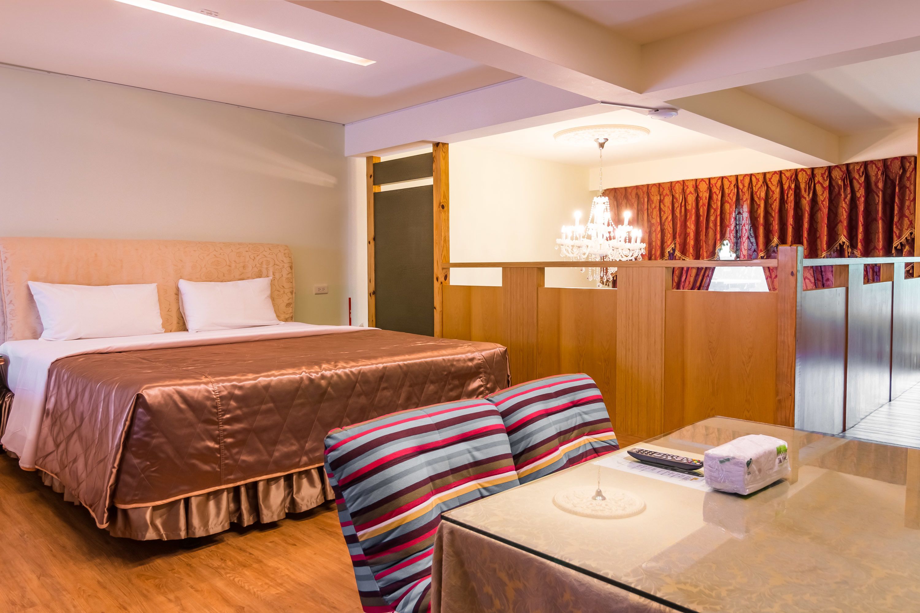A hotel room with a large bed, a small table with a remote control, and a chandelier.
