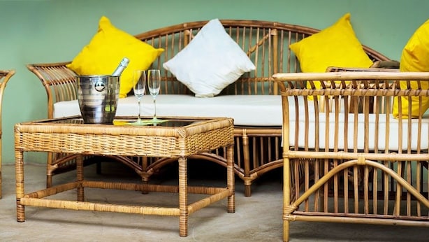 A wicker sofa set with yellow cushions, a metal bucket, and two glasses on a woven table. - The Father's Hotel (Accra)