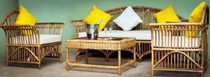 A wicker sofa set with yellow cushions, a metal bucket, and two glasses on a woven table. - The Father's Hotel (Accra)