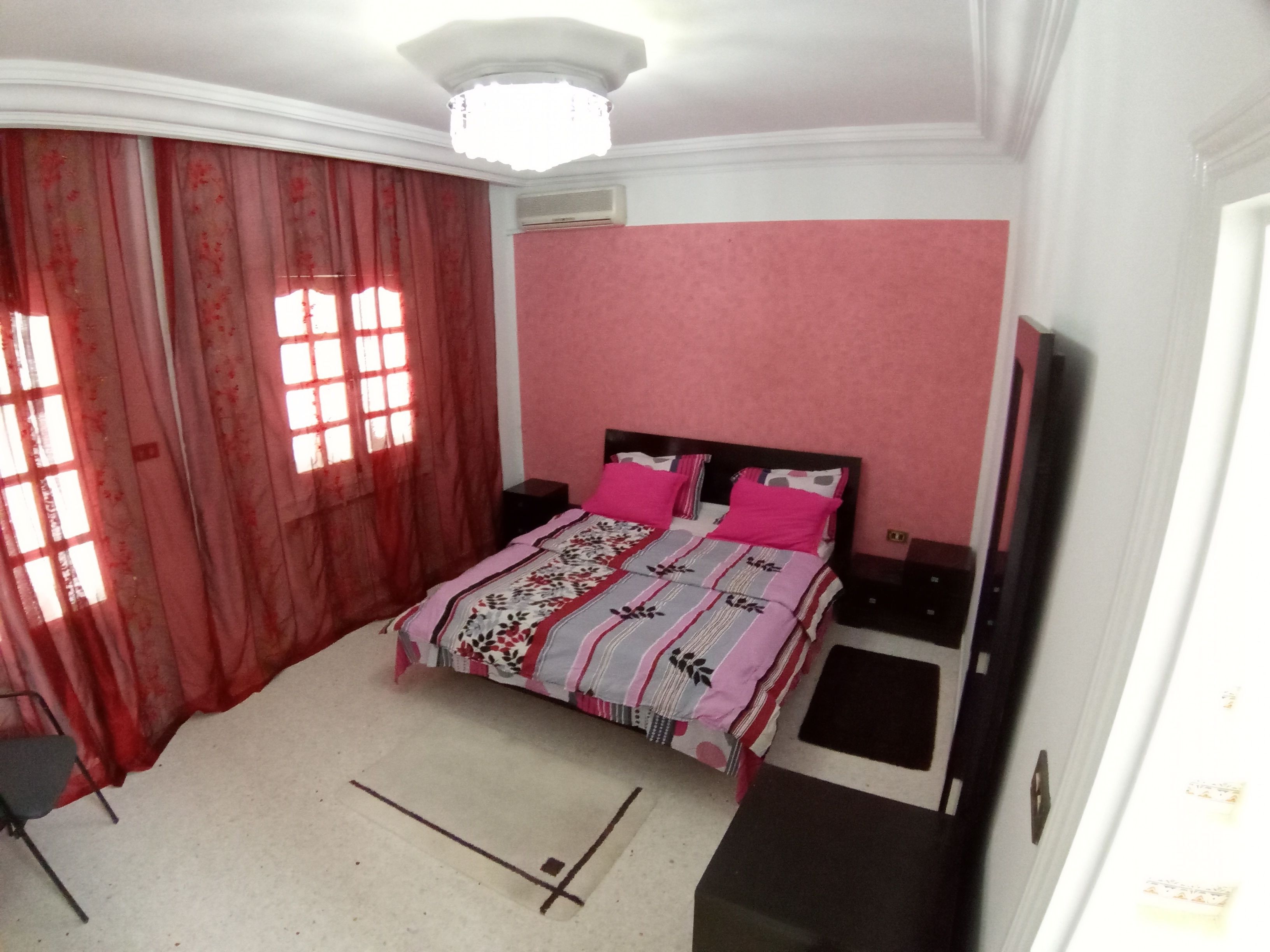A bedroom with a bed, curtains, a ceiling light, and a wall-mounted air conditioner.