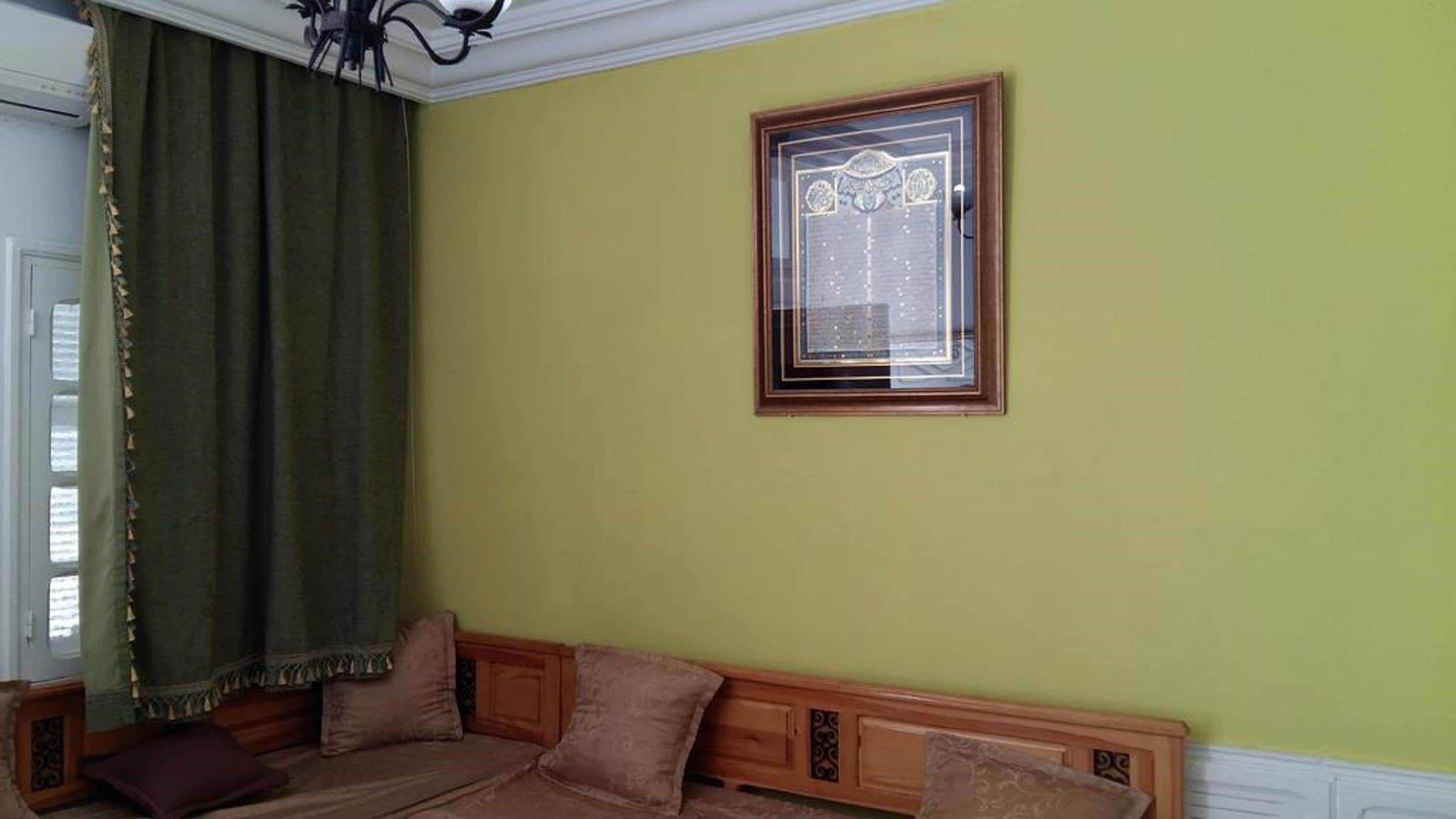 A room with a green wall, a wooden sofa with cushions, and a framed picture.