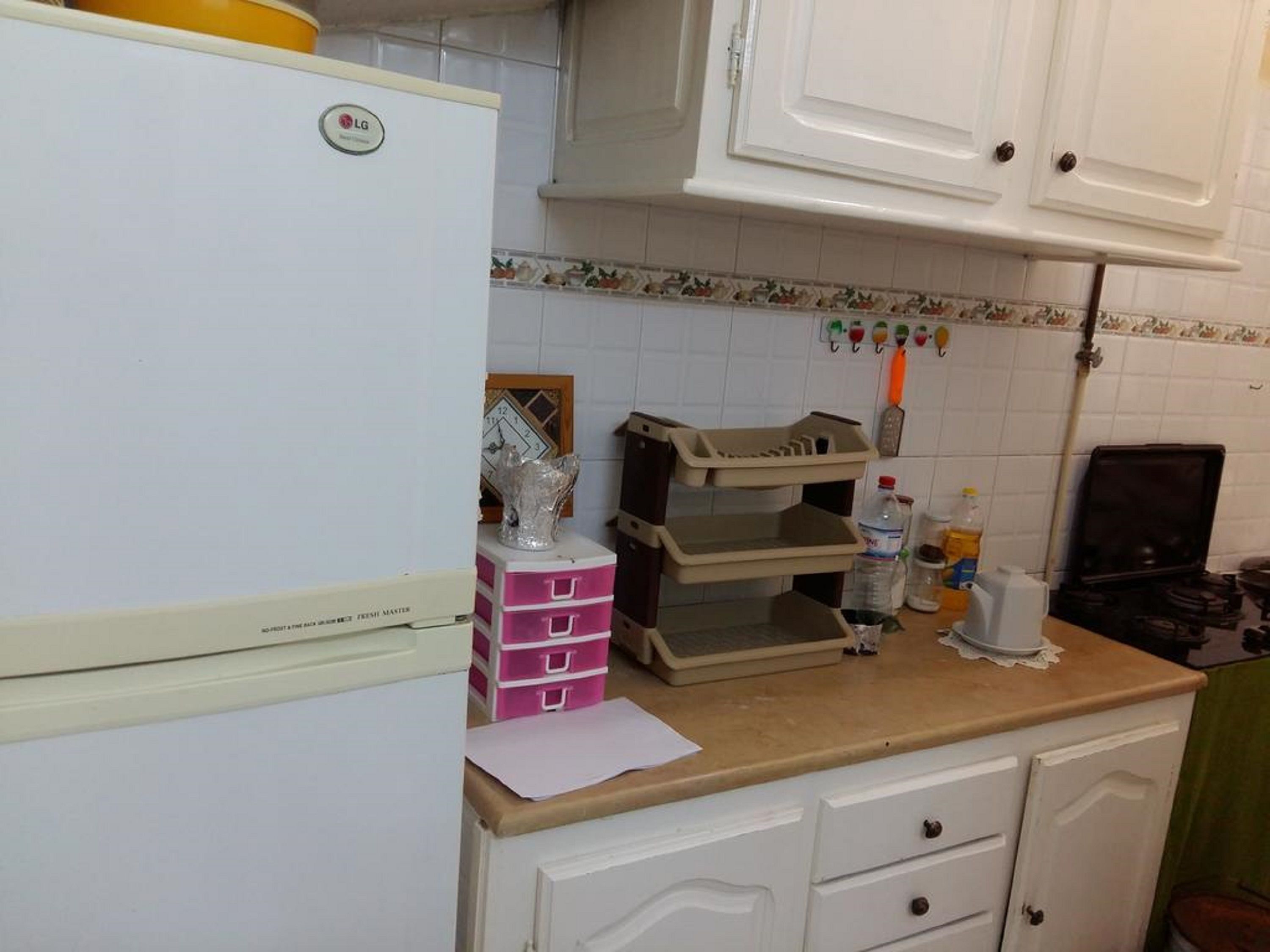 A kitchen with white cabinets, a white refrigerator, a countertop with various items, and a tiled backsplash.