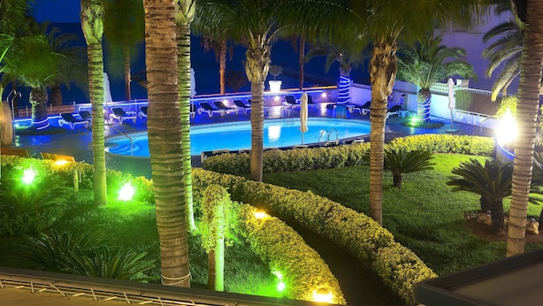A pool area with lounge chairs and palm trees, surrounded by well-lit hedges and pathways. - Miami Mar - Boutique Hotel & Restaurant (Sant Carles de la Rapita)