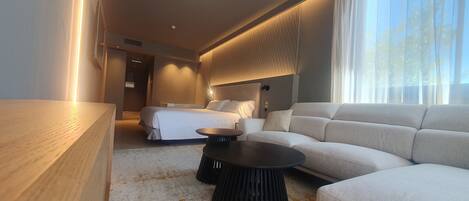 Una habitación de hotel moderna con una cama grande, un sofá, una mesa de centro y una mesita de noche de madera.