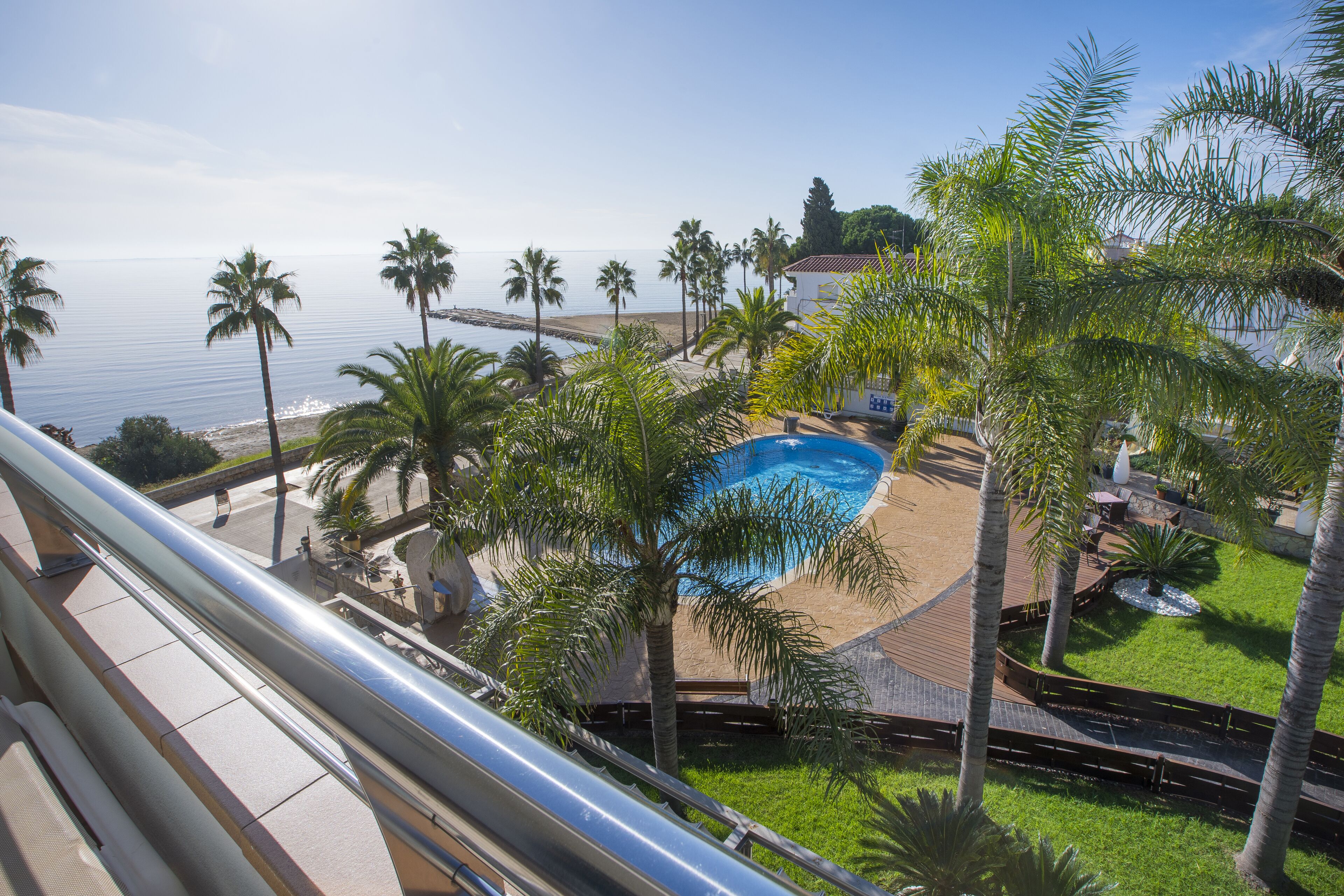 A pool area with palm trees, a view of the sea, and a building in the background.